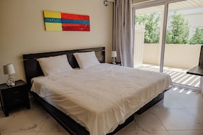 A bedroom with a bed, nightstands, a lamp, a window with curtains, and a colorful artwork on the wall.