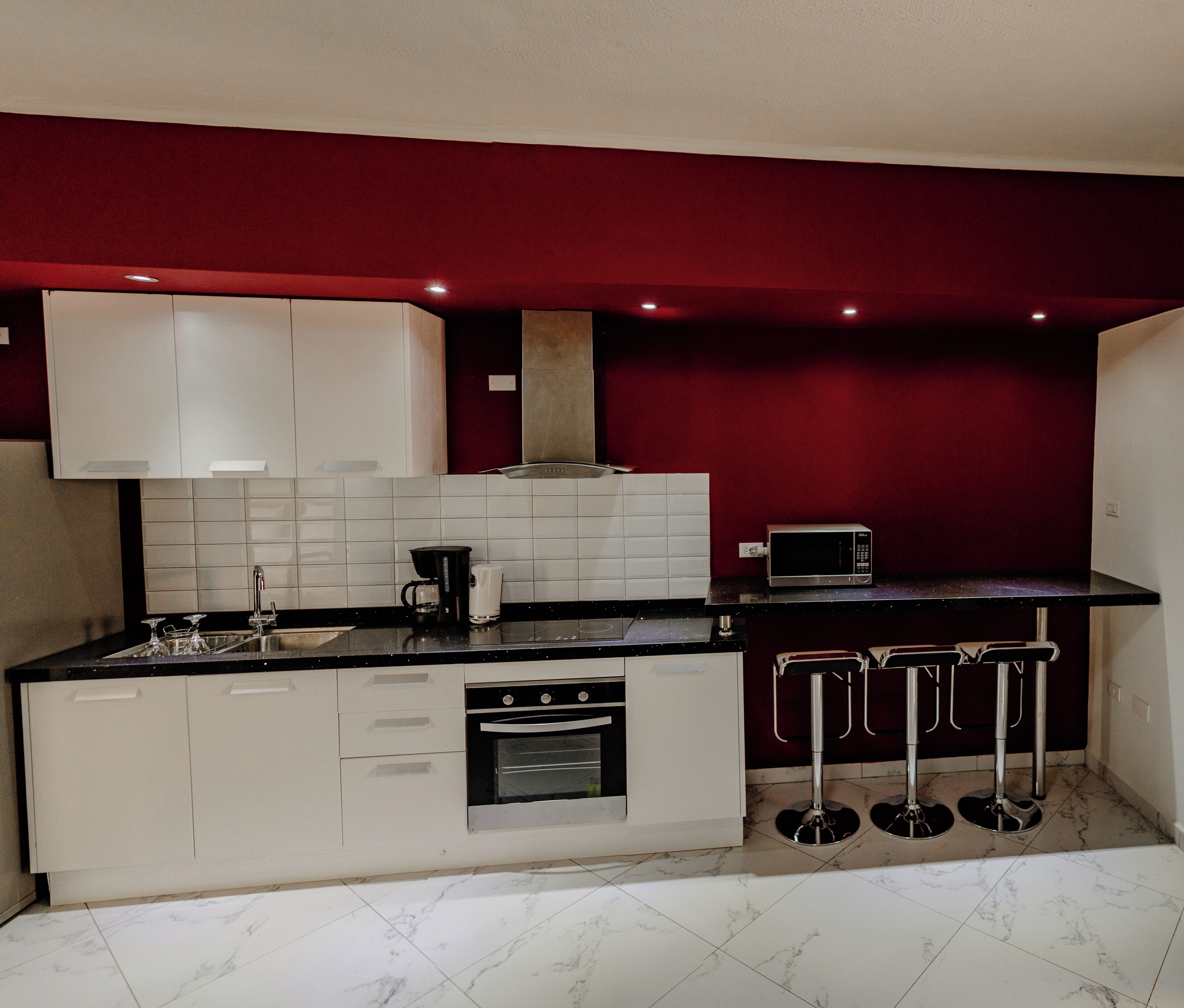A compact kitchen with white cabinets, a built-in oven, a coffee maker, and a microwave.
