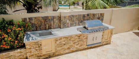 An outdoor kitchen with a stone backsplash, a built-in grill, and a sink.