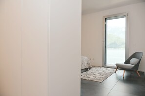 Quarto moderno com uma cama, uma cadeira e vista pela ampla janela.