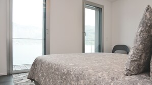 Une chambre à coucher avec un lit, une chaise et une vue sur une étendue d’eau, visible à travers une porte.