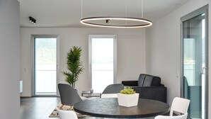 Un espace repas moderne avec une table ronde, des chaises blanches, une plante en pot et un canapé noir.