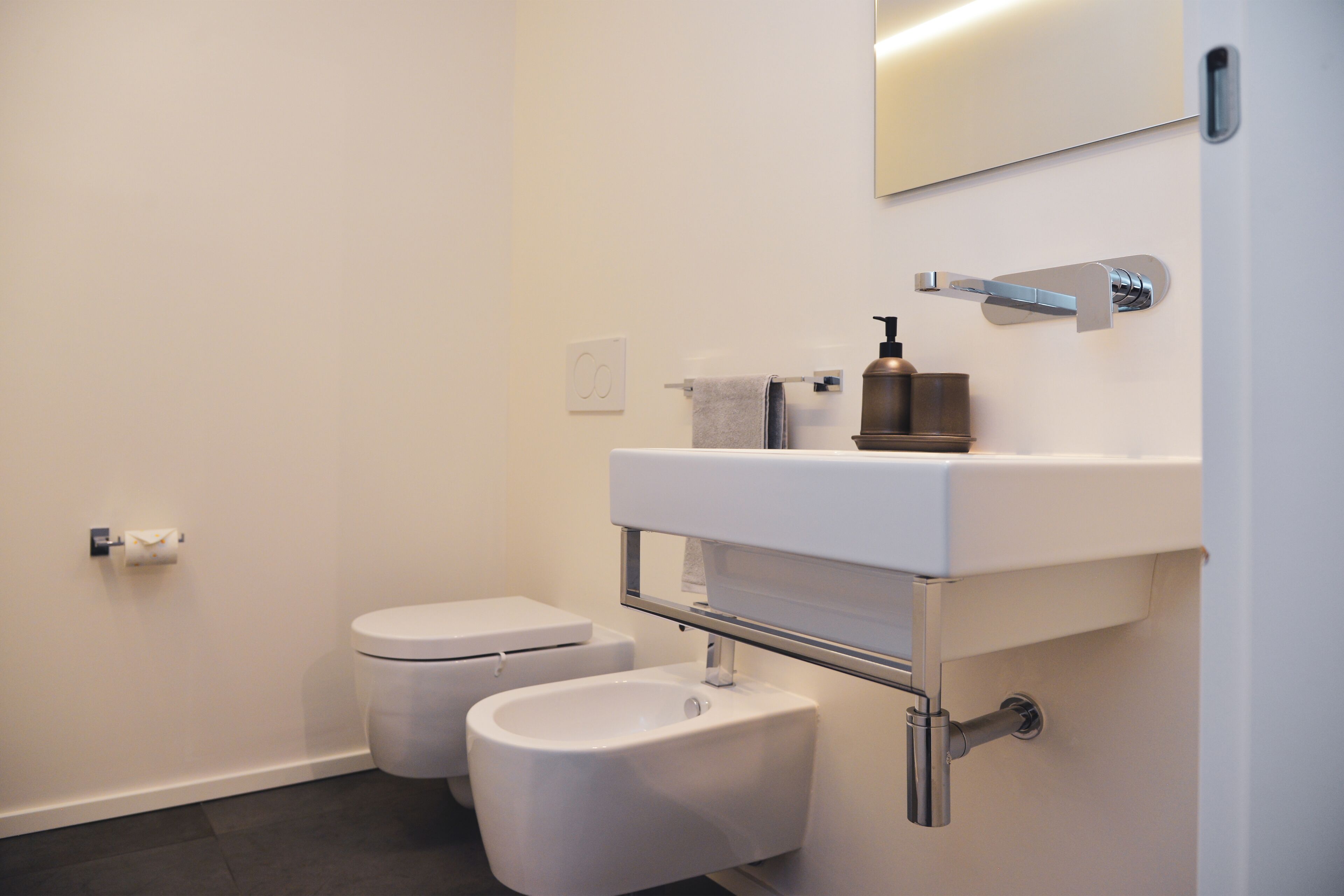 A modern bathroom with a toilet, bidet, and a sink with a mirror above.