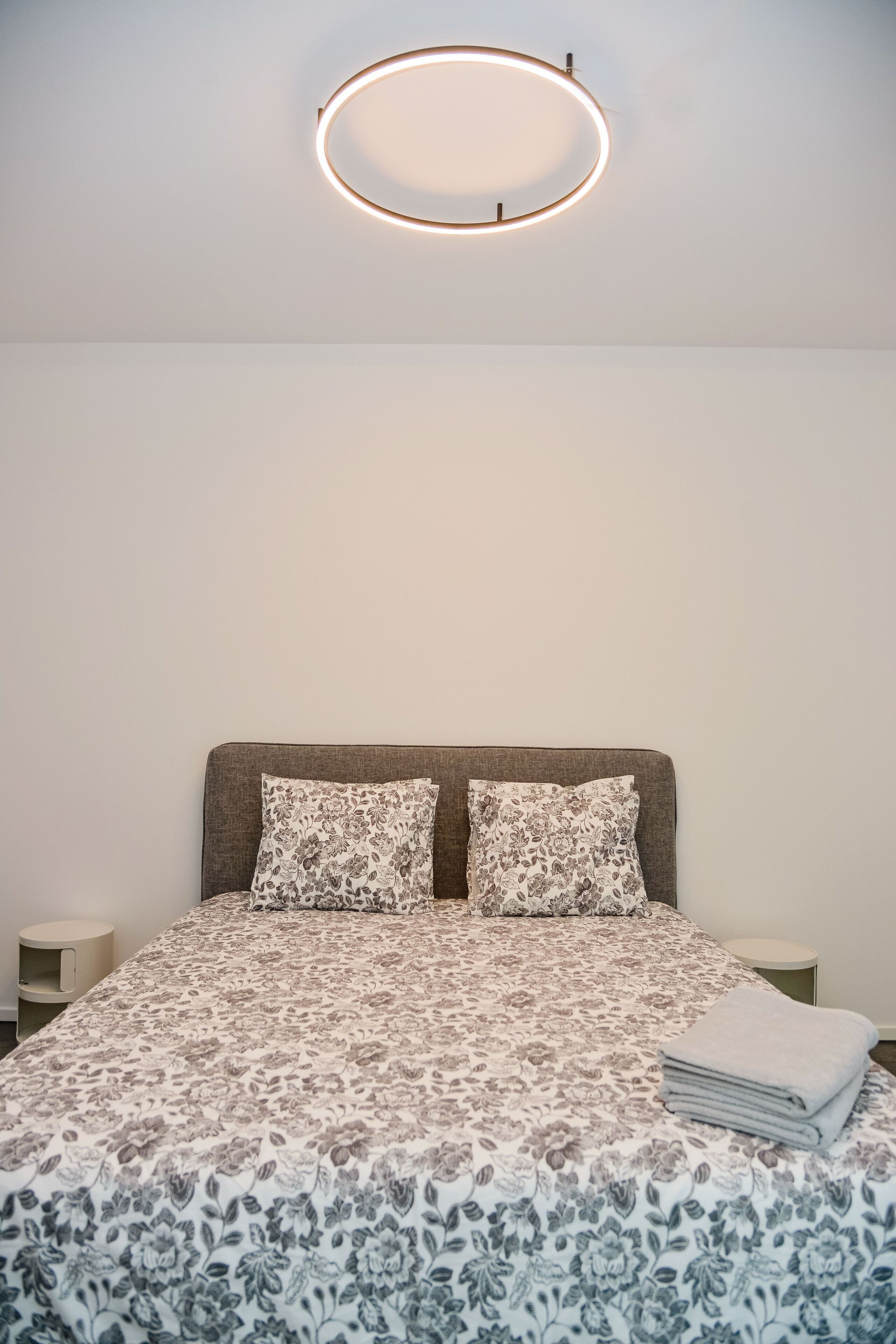 A neatly made bed with a floral-patterned bedspread, two pillows, and a folded towel on the side.
