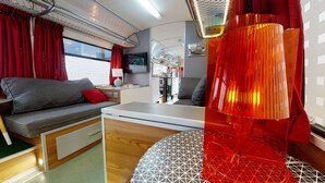 A cozy interior with a sofa, a small table, and a lamp. - Gozo Bus Glamping - Stay on a 1974 Vintage Maltese bus in Xlendi (Munxar)