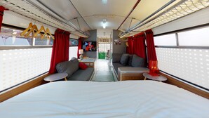 A train interior with a bed, seating area, and a small table. - Gozo Bus Glamping - Stay on a 1974 Vintage Maltese bus in Xlendi (Munxar)
