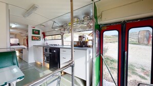 A compact kitchen with a sink, stove, and a coffee machine. - Gozo Bus Glamping - Stay on a 1974 Vintage Maltese bus in Xlendi (Munxar)