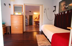 Cozy bedroom with a dresser, mirror, and comfortable bed, leading to a dining area with a table and chairs.