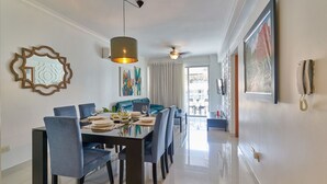 A modern dining area with a long table, blue chairs, and a ceiling fan. - Apto En Zona Privilegiada De Santo Domingo City (Santo Domingo)
