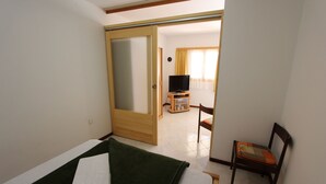 Una camera d'albergo con un letto, una TV su un mobile, una sedia e una porta che dà su un'altra stanza.