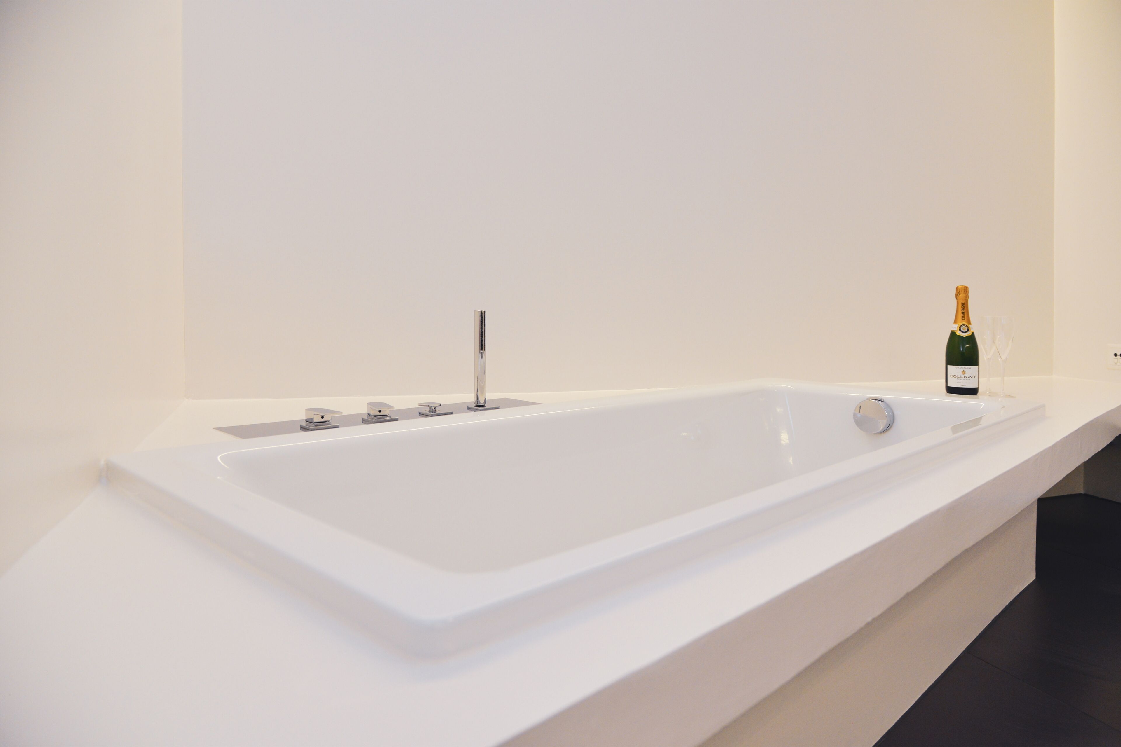 A modern bathroom with a large white bathtub, a bottle of champagne, and a single faucet.