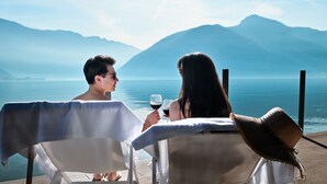 Duas pessoas sentadas à mesa com vista para um lago e montanhas.