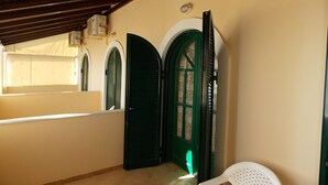 Un pasillo con una puerta verde, una silla blanca y un ventanal con vistas.