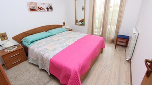 A bedroom with a bed, a nightstand, a chair, a window with curtains, and a radiator. - Liliana One-bedroom Apartment (Rovinj)