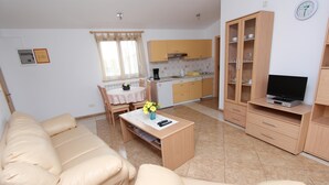 A living room with a beige sofa, a coffee table with a vase of flowers, a TV on a stand, and a kitchen in the background. - Liliana One-bedroom Apartment (Rovinj)