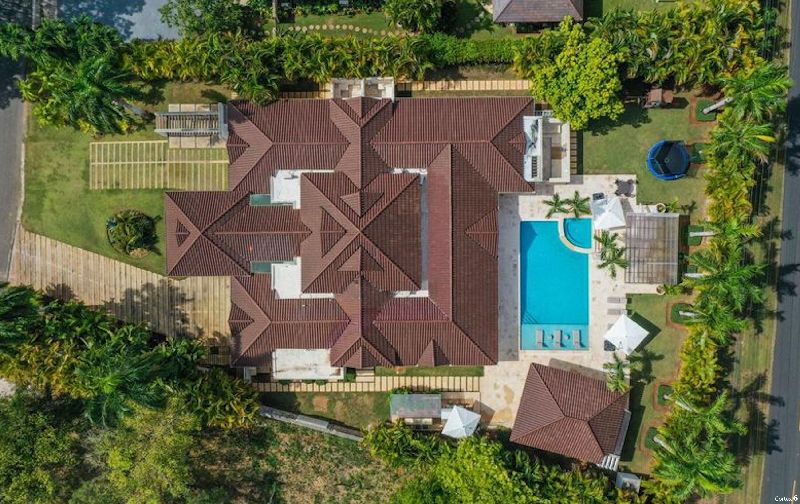 An aerial view of a residential property with a swimming pool, multiple roof structures, and surrounding greenery.