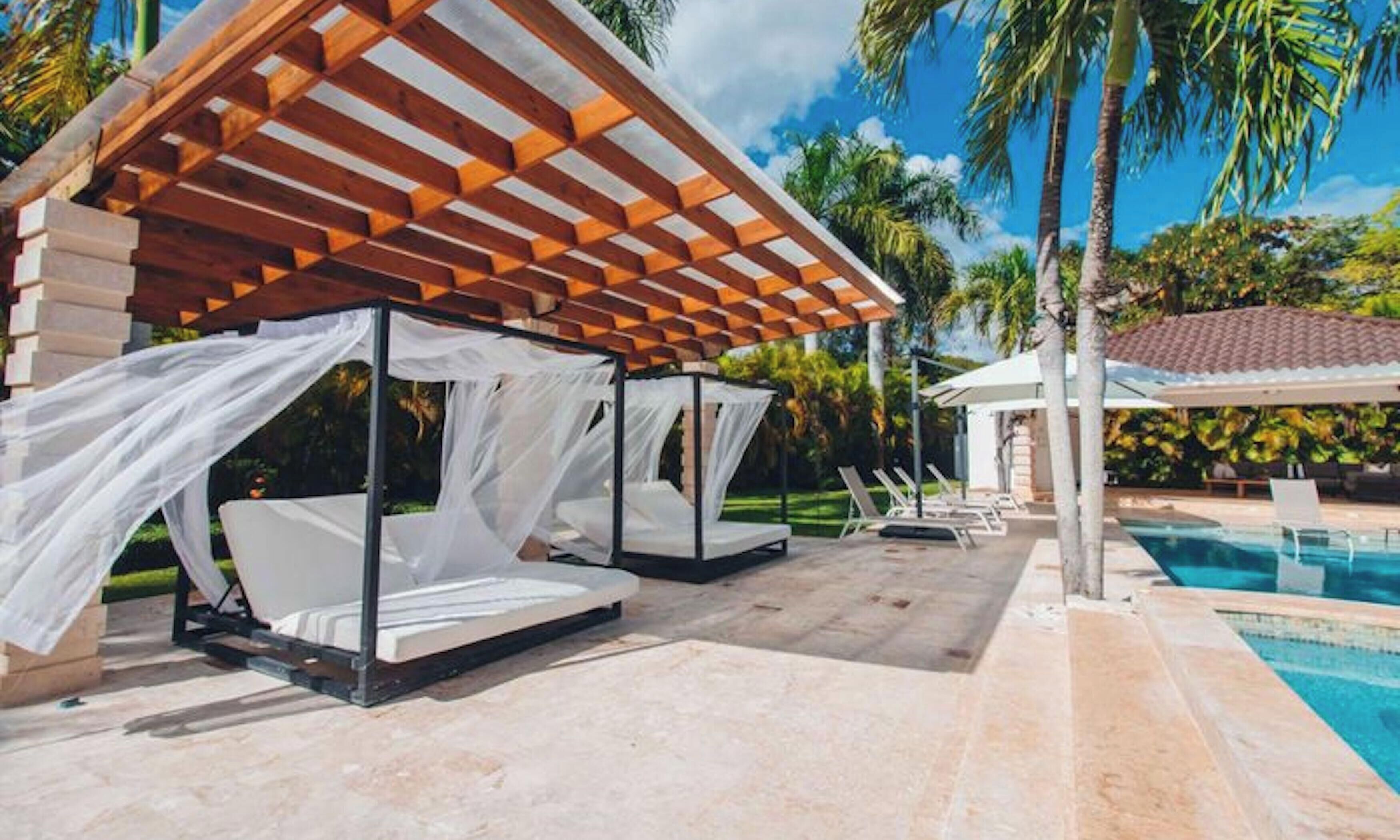A poolside area with two white canopy beds and lounge chairs.