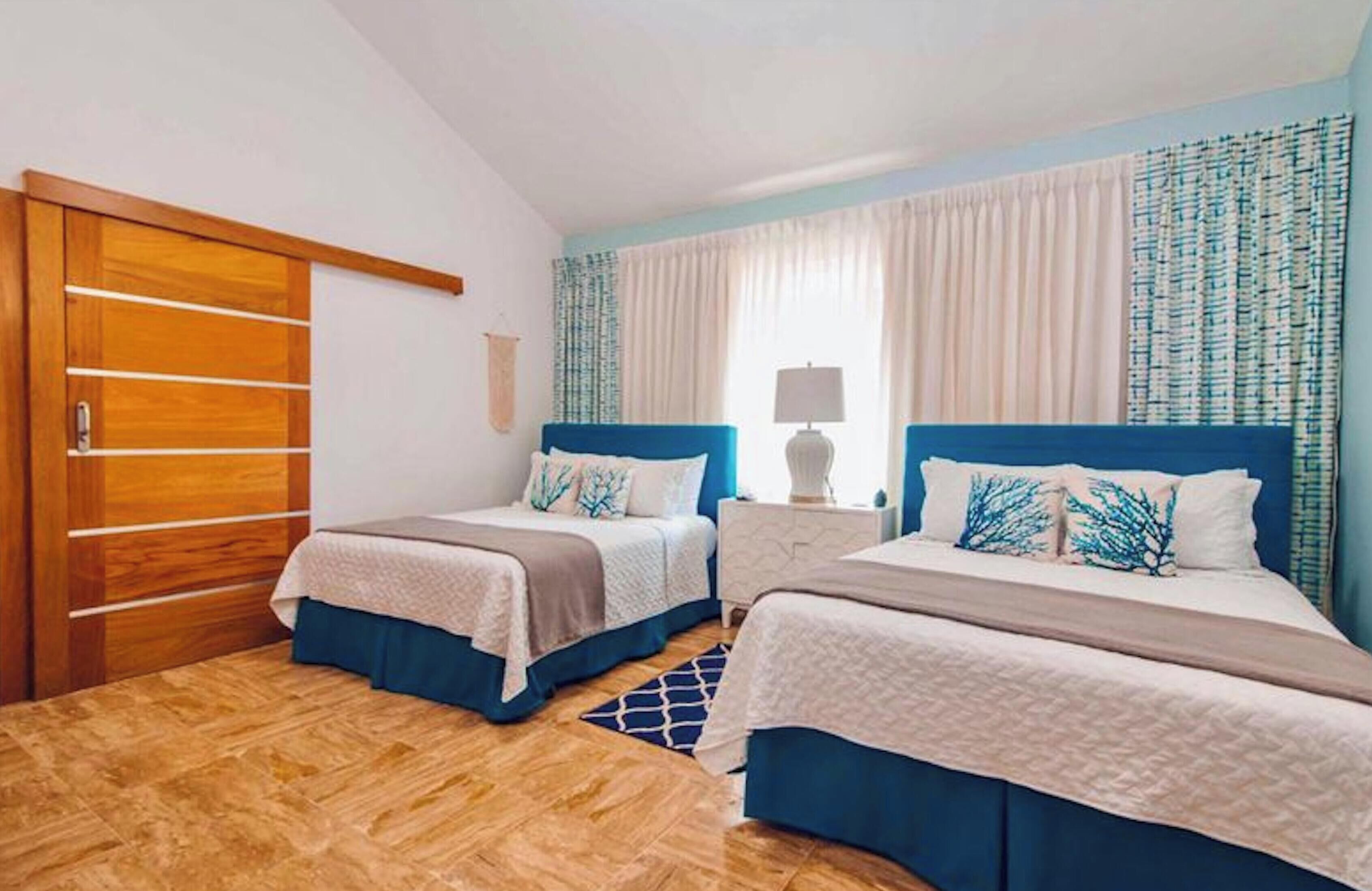 A hotel room with two beds, a wooden wardrobe, and a window with curtains.