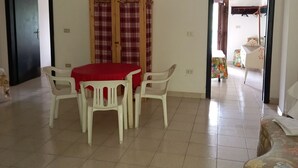 A room with a dining table and chairs, a wardrobe, and a bed.