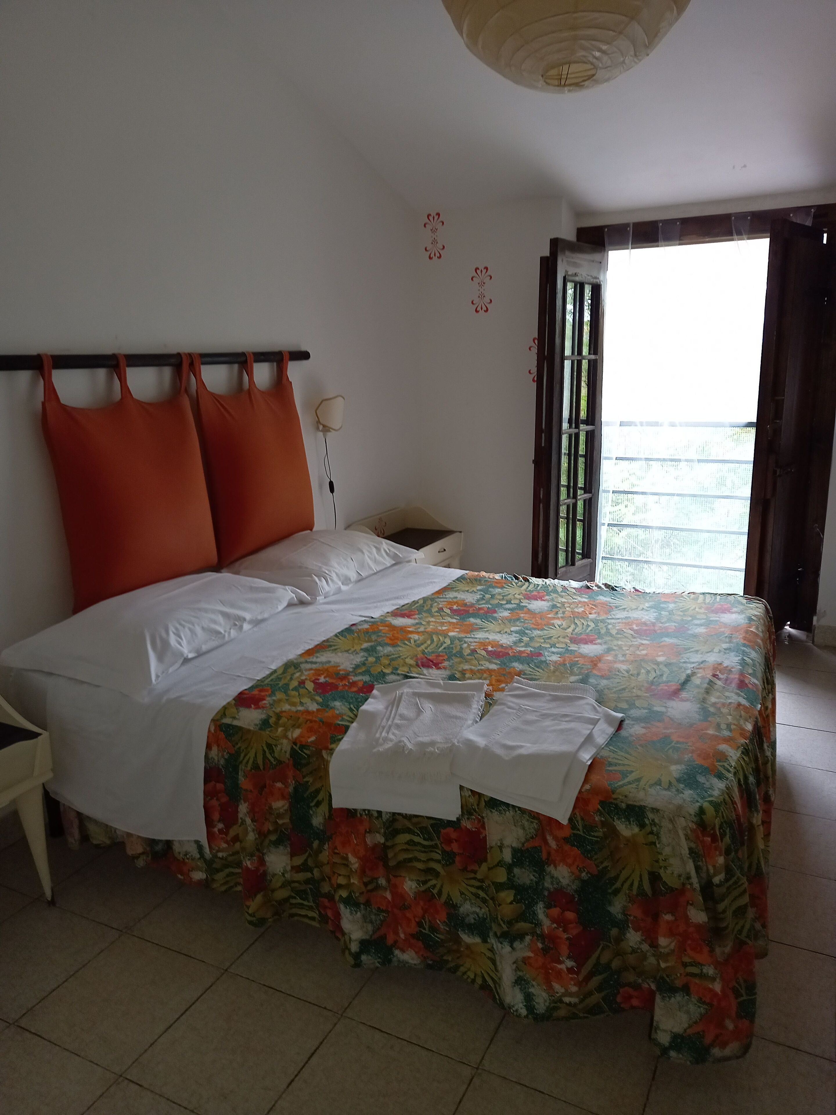 A bed with a floral bedspread, a nightstand, a lamp, and a window with a view.