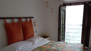 A bed with a floral bedspread, a nightstand, a lamp, and a window with a view.