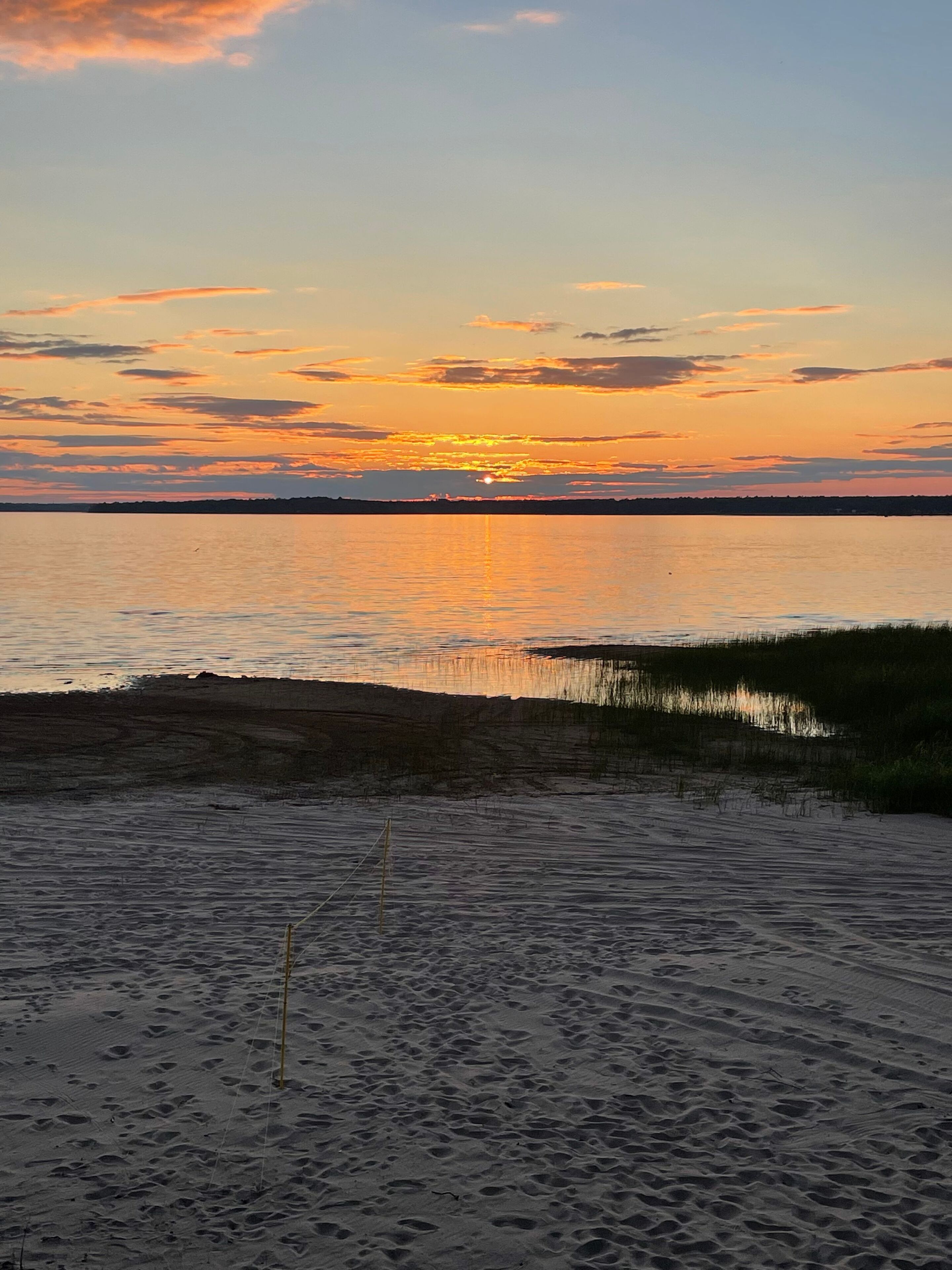 Ein Strand mit freiem Blick auf den Sonnenuntergang über dem Wasser.