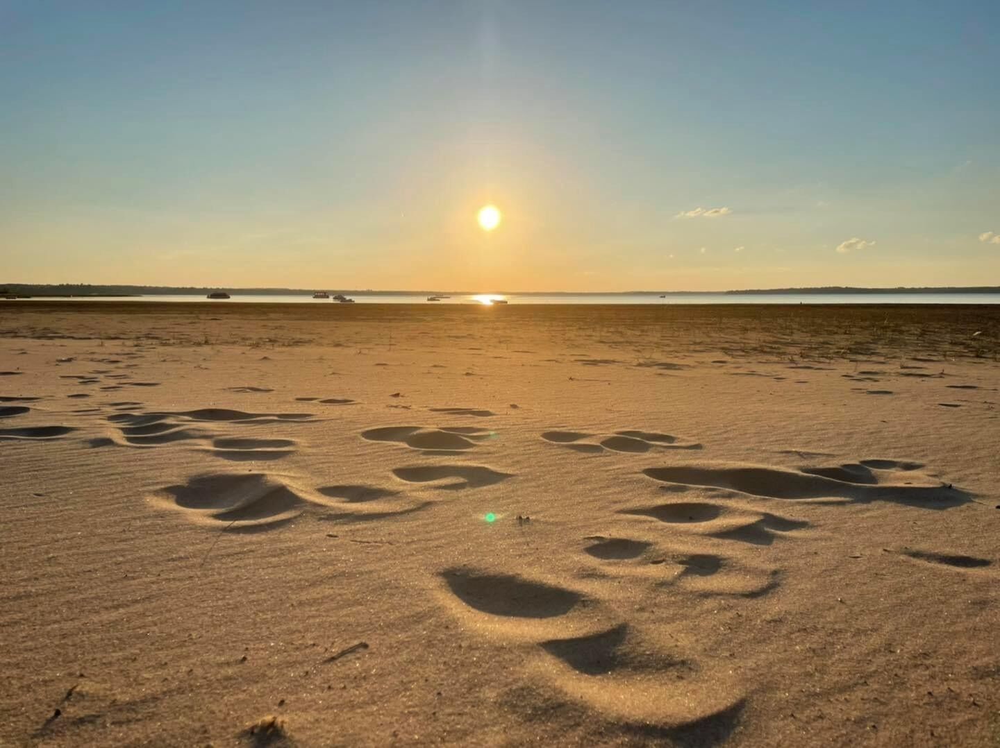 Een strand met voetafdrukken in het zand en een ondergaande zon in de verte.