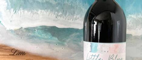 Una botella de vino con la etiqueta "The Little Blue Beach House Cabernet Sauvignon" colocada frente a una tabla de madera con el mismo nombre.