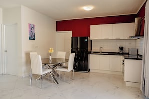 A modern kitchen with white cabinets, a black refrigerator, and a dining area with a glass table and white chairs.