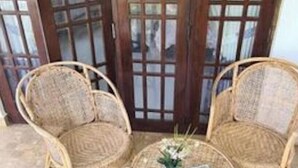 Ein überdachter Patio-Bereich mit zwei Korbstühlen und einem kleinen runden Tisch, mit Blick durch große Glasfenstertüren.