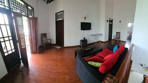 Ein geräumiges Wohnzimmer mit einer Couch, einem Fernseher und Holzboden.