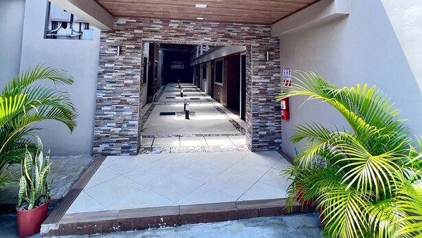 A modern building entrance with a covered walkway, stone accents, and potted plants. - Tuareg Place Aeropuerto A,C (Alajuela)