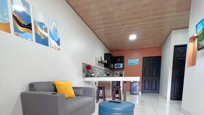 A spacious living area with a grey sofa, a blue ottoman, and a kitchen area with a microwave and cabinets. - Tuareg Place Aeropuerto A,C (Alajuela)