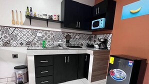 A modern kitchen with black cabinets, a microwave, and a refrigerator. - Tuareg Place Aeropuerto A,C (Alajuela)