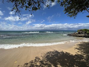 A beach with clear water, waves, and a rocky outcrop.