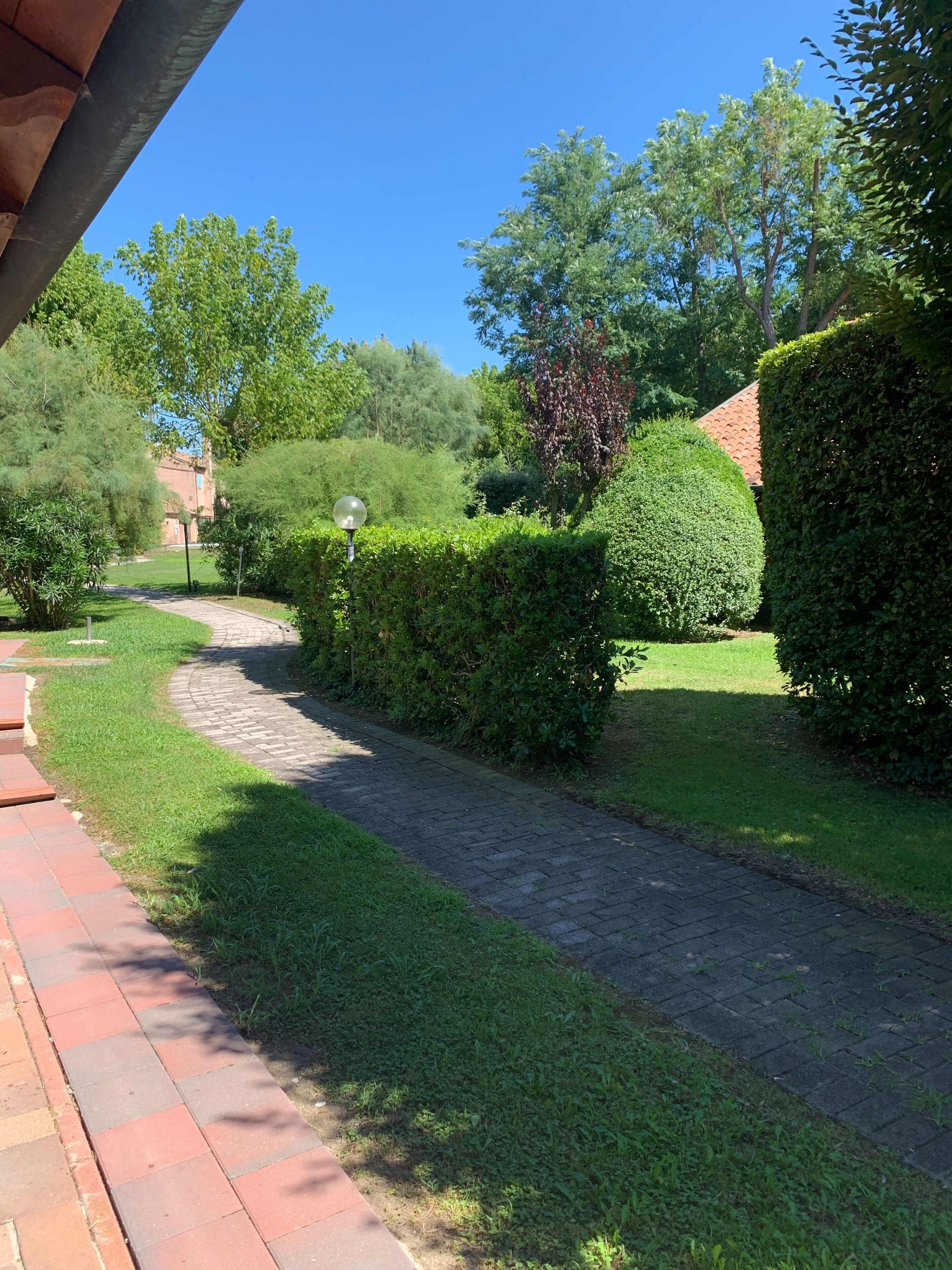 Un chemin pavé traverse un jardin bien entretenu, agrémenté de haies soigneusement taillées et d’une variété d’arbres.