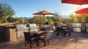 An outdoor patio with a grill, dining table, chairs, and umbrellas.