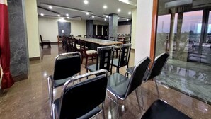 Uma sala de conferências com uma mesa comprida e várias cadeiras, uma cortina vermelha e uma vista através de um painel de vidro.