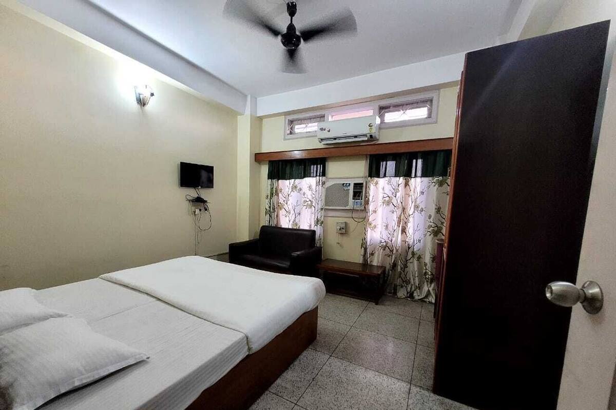 A room with a bed, a chair, a ceiling fan, an air conditioning unit, and a door.