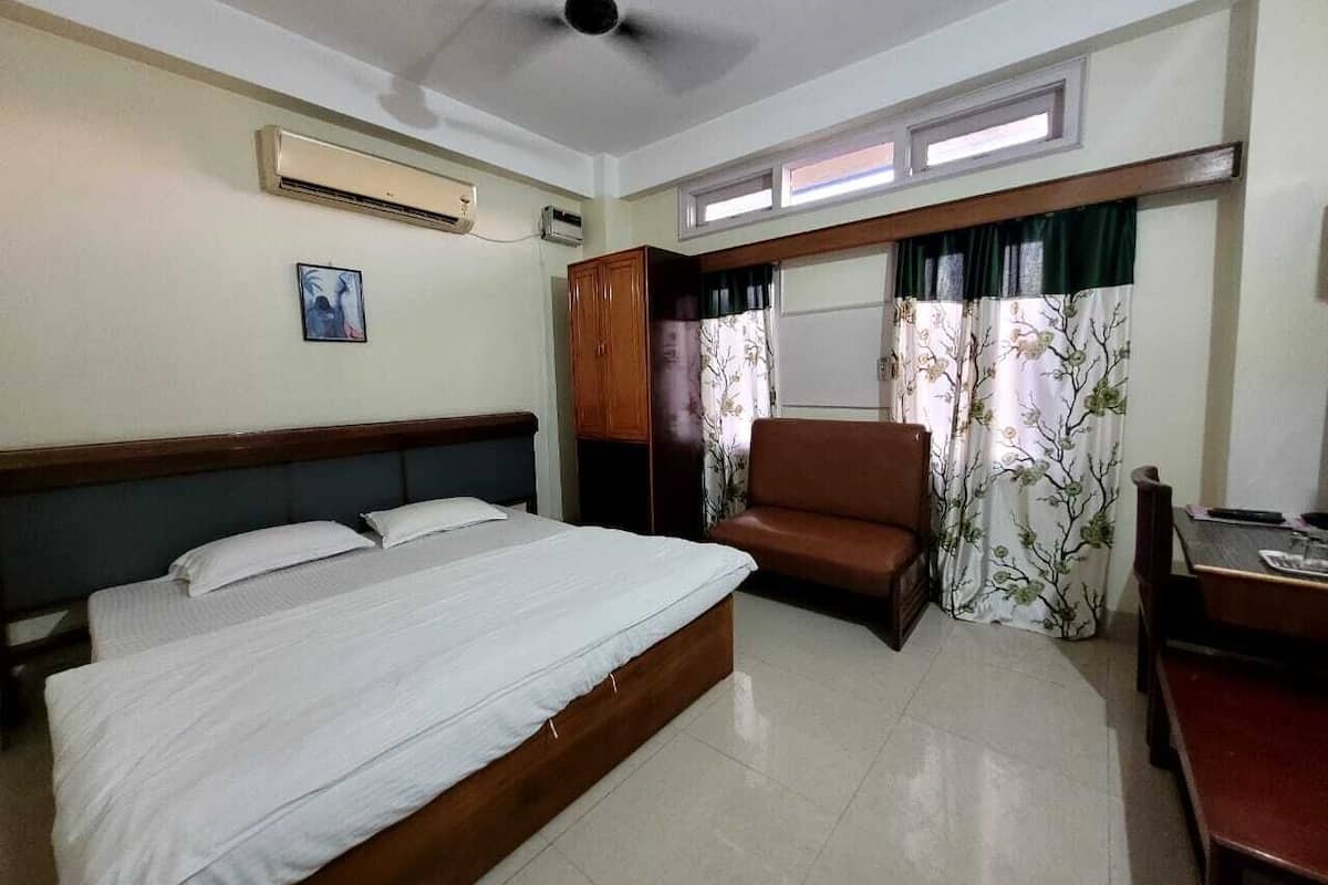 A hotel room with a bed, a chair, a desk, and a window with curtains.