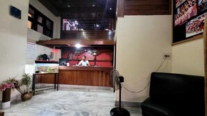 Uma área de recepção com piso de mármore, um sofá preto, uma mesa com uma pessoa e um painel de fotos na parede.