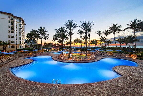 Ein Poolbereich eines Resorts mit Liegestühlen, Palmen und einem Gebäude im Hintergrund.