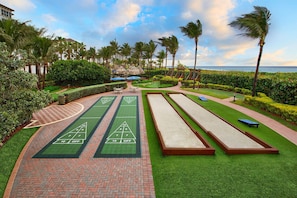 Una cancha de croquet con césped verde y carriles numerados, rodeada de palmeras y vistas al océano.