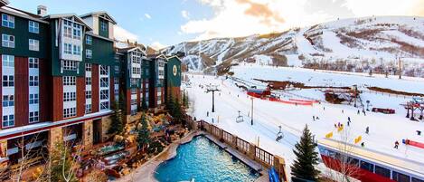 A hotel with a pool, ski slopes, and a mountain backdrop.