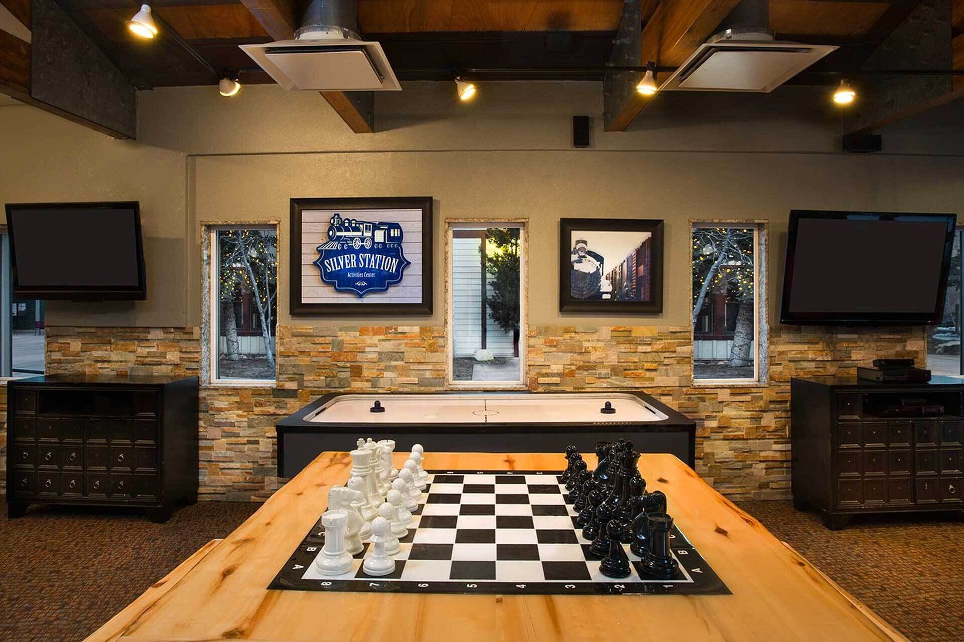Une pièce avec une table en bois préparée pour une partie d’échecs, des murs en pierre et des tableaux encadrés accrochés au mur.