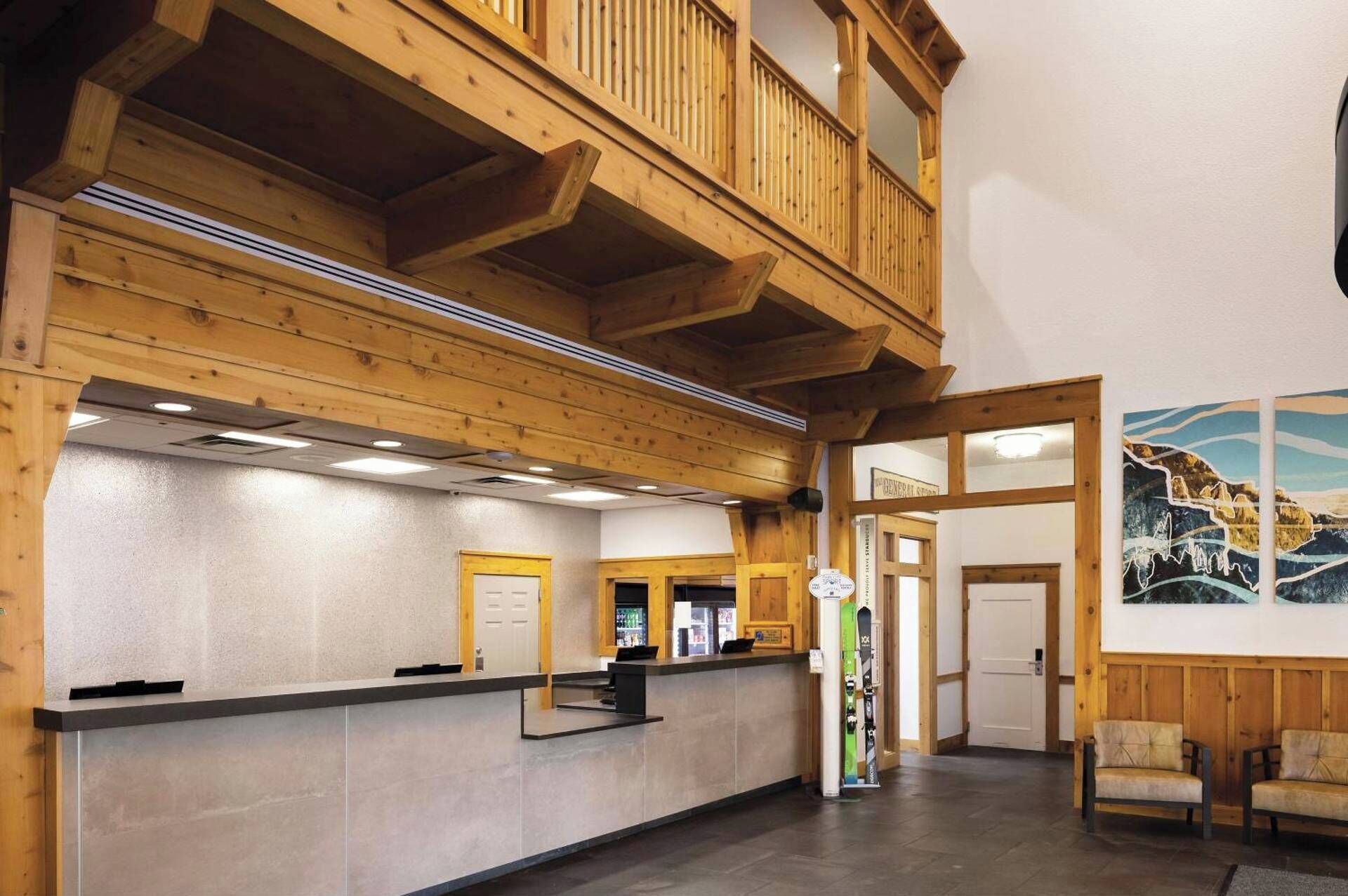 A reception area with a wooden reception desk, a balcony, and a wall with a mountain painting.