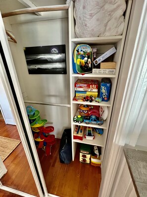 Storage area with shelves and a variety of items, including a backpack, picture, toy cars, and a toy train set.