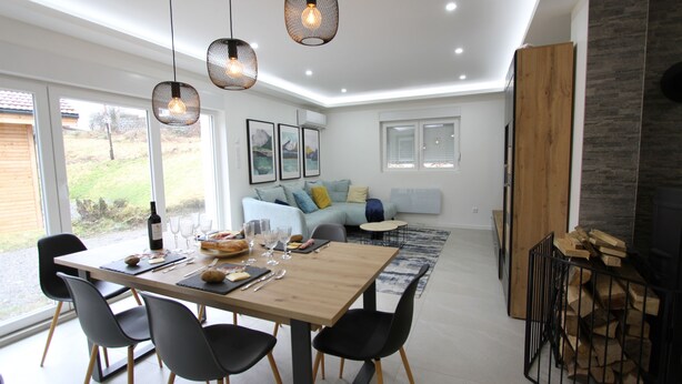 A modern dining area with a wooden table, black chairs, and hanging pendant lights. - Maison Cossue, Moderne et Calme à La Bresse 5 Chbr (La Bresse)