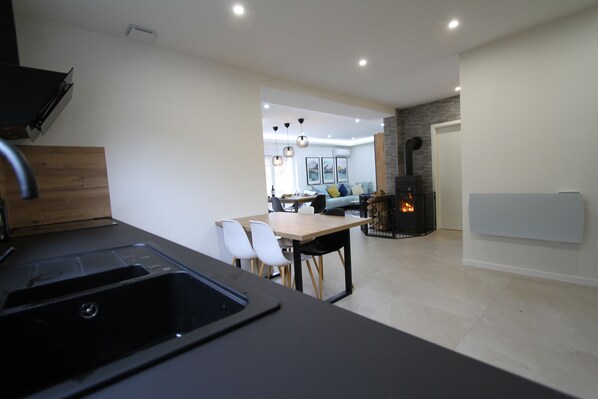 A modern kitchen with a built-in sink, a dining area with chairs, and a fireplace in the background.