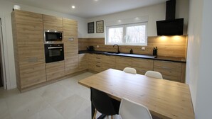 A modern kitchen with wooden cabinets, a built-in oven, a microwave, and a dining area with two chairs. - Maison Cossue, Moderne et Calme à La Bresse 5 Chbr (La Bresse)